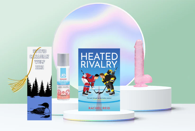 picture of book heated rivalry with a 6" pink dildo, a bottle of warming lubricant and a custom bookmark